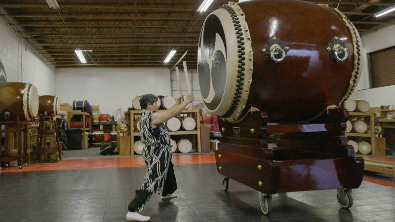 A woman dressed in traditional taiko player attire is about to hit a huge drum with a pair of wooden sticks.