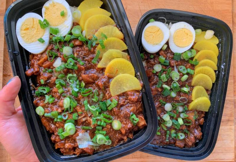 Two takeout containers of lu rou fan, or Taiwanese braised pork rice, garnished with yellow daikon pickles and hard-boiled eggs.
