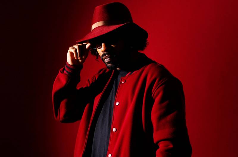 A man in a red fedora, against a red background, wearing a red jacket