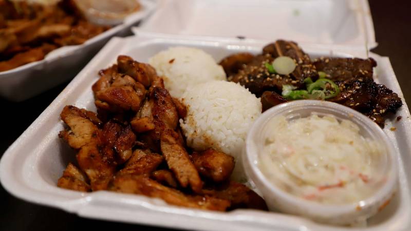 Hawaiian plate lunch with grilled chicken, short ribs, macaroni salad, and rice in a Styrofoam container.