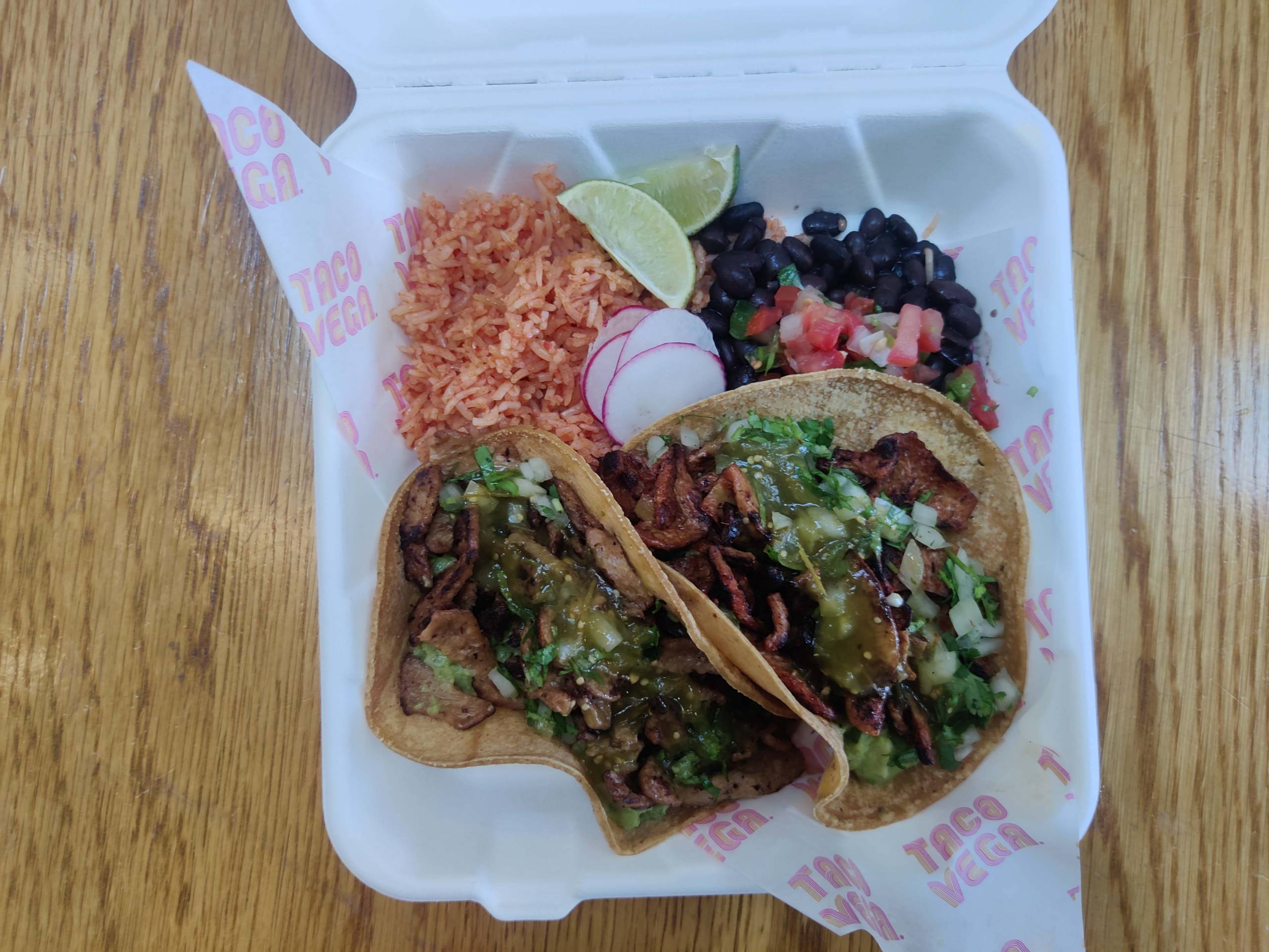A styrofoam container with three tacos, rice, and beans.