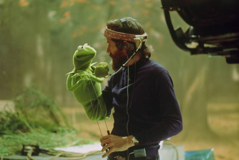 A male puppeteer holds a Kermit the Frog puppet on the set of a movie