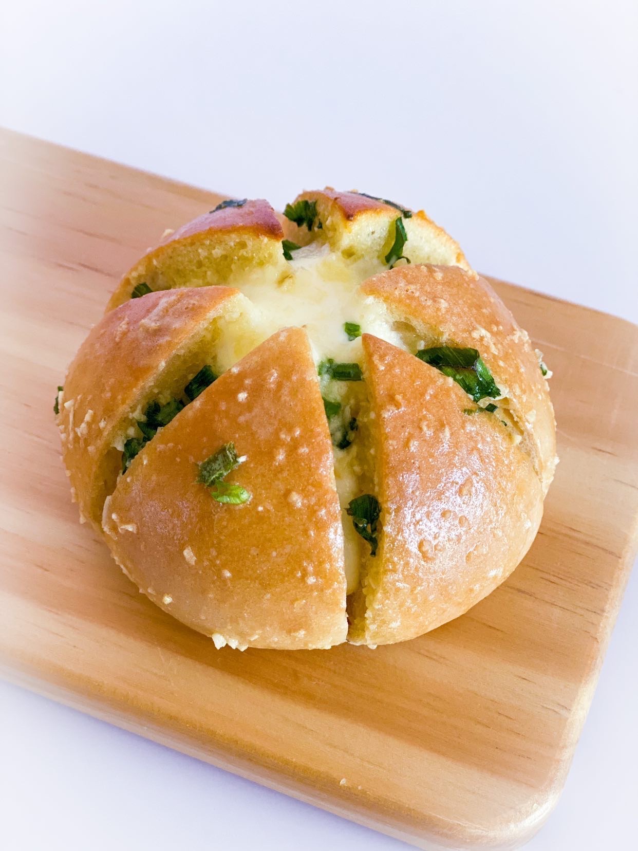 Scallion garlic cream cheese bun on a wooden cutting board, with the bun's oozy cream cheese interior visible.
