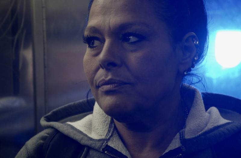 A woman with a concerned look on her face is shot in low light in a still from a documentary.