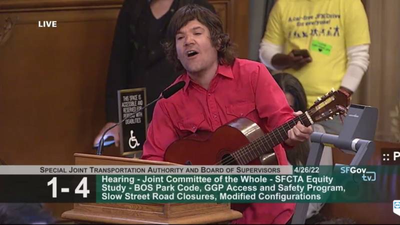 A man in a red shirt and guitar sings a song at the podium