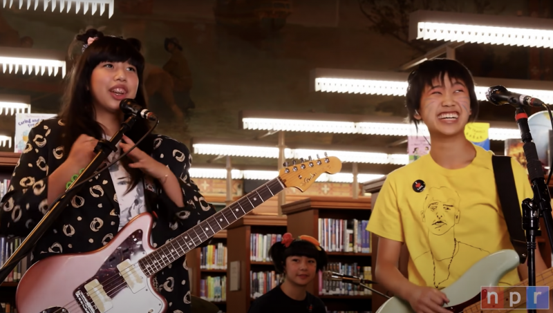 A still from a concert by a punk rock quartet of young Asian-American women inside a library.