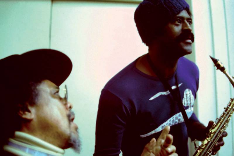 Mingus with goatee and hat and glasses, and McPherson, holding a saxophone, in a beanie