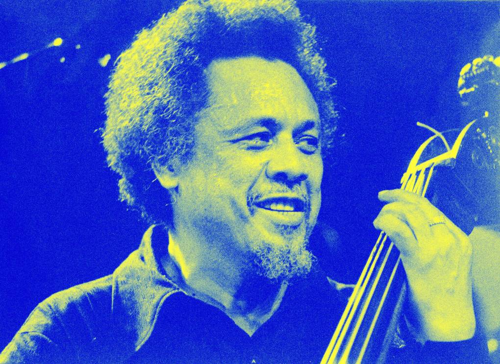 Charles Mingus playing the bass, looking to the right and smiling knowingly