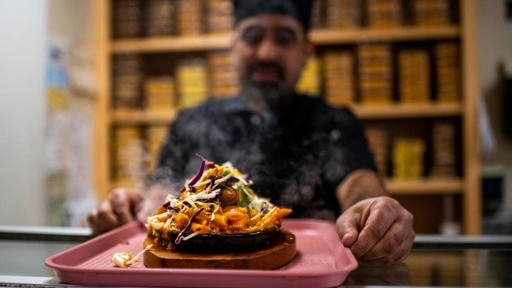 An employee holds out a samosa sizzler, billowing with smoke, on a pink tray.