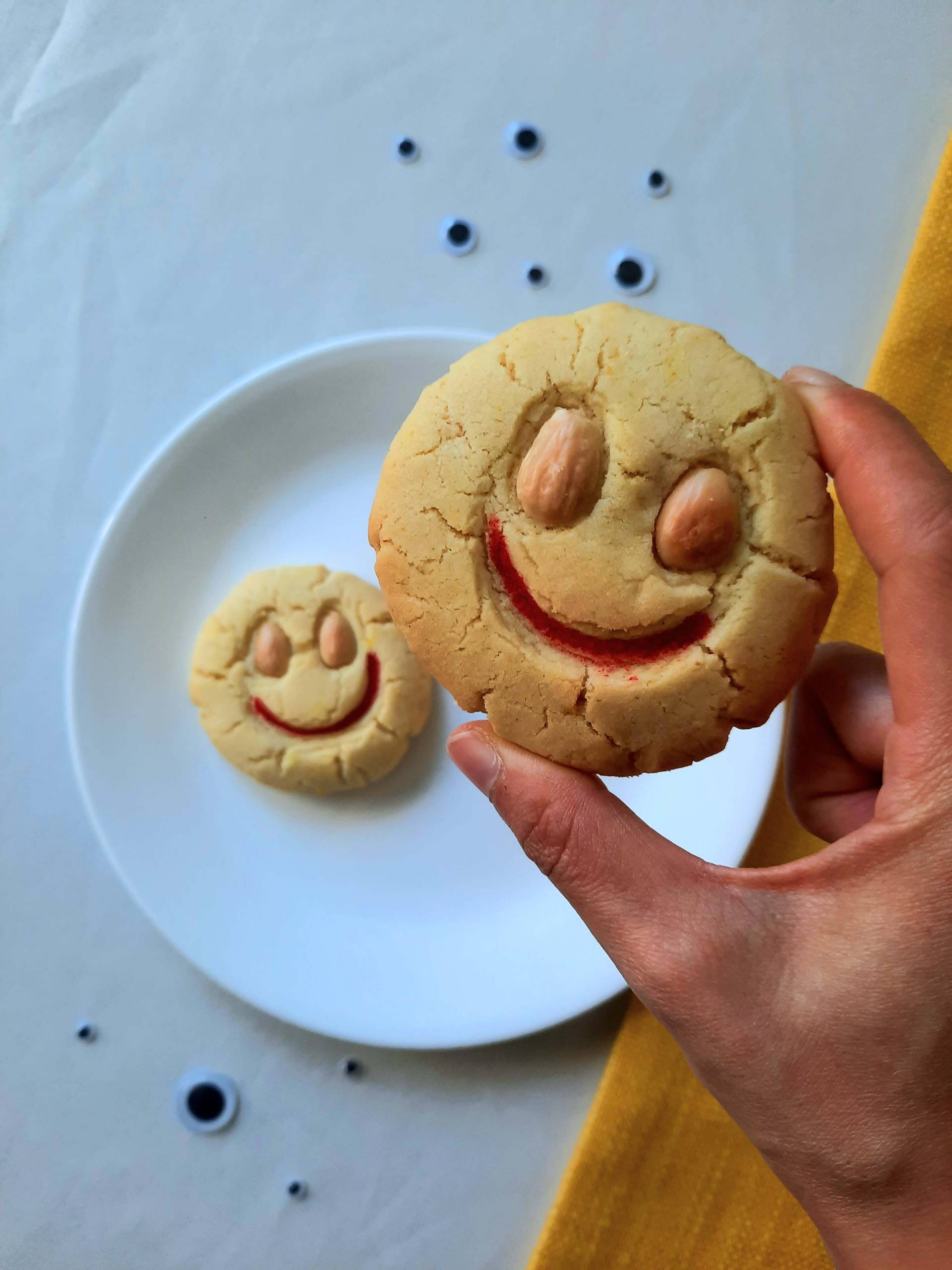 A hand holding a smiley-face almond cookie, with two almonds serving as the eyes.