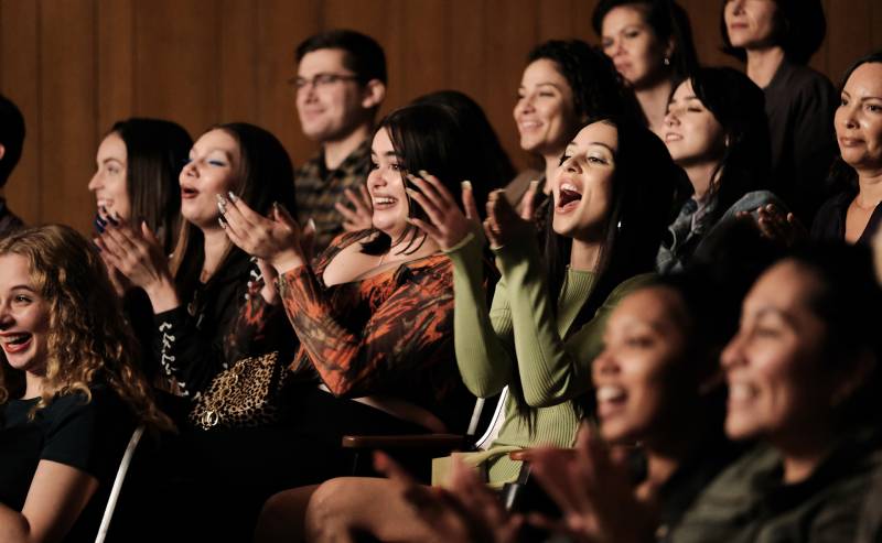 A group of teens clap and cheer in an auditorium