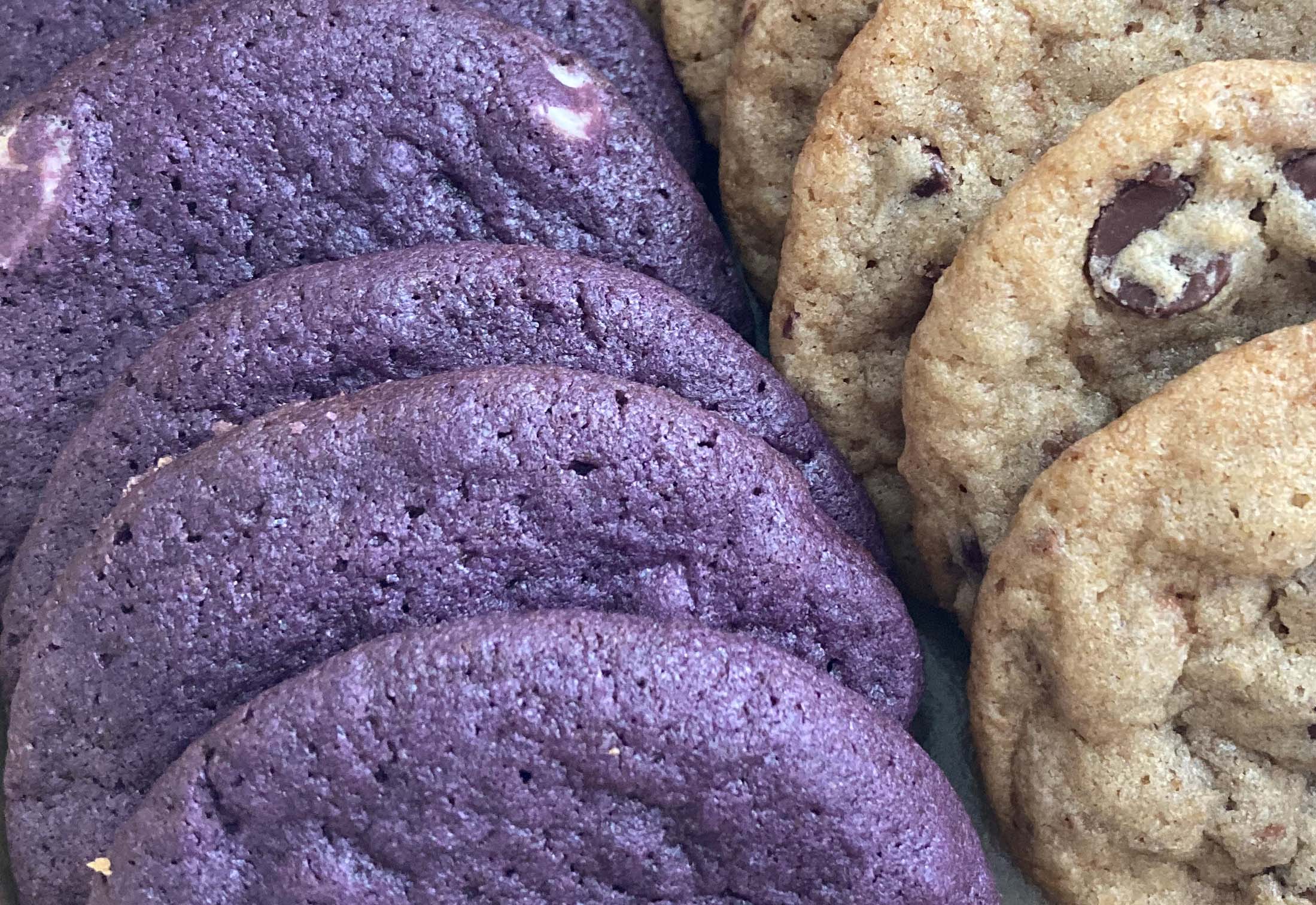 Close-up photo of a box of chocolate chip cookies, with a row of bright purple ube white chocolate cookies on the left and more conventional-looking chocolate chip cookies on the right.