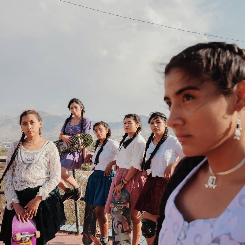 Six young women stand in a row, determined expressions on their faces, mountains visible in the distance.