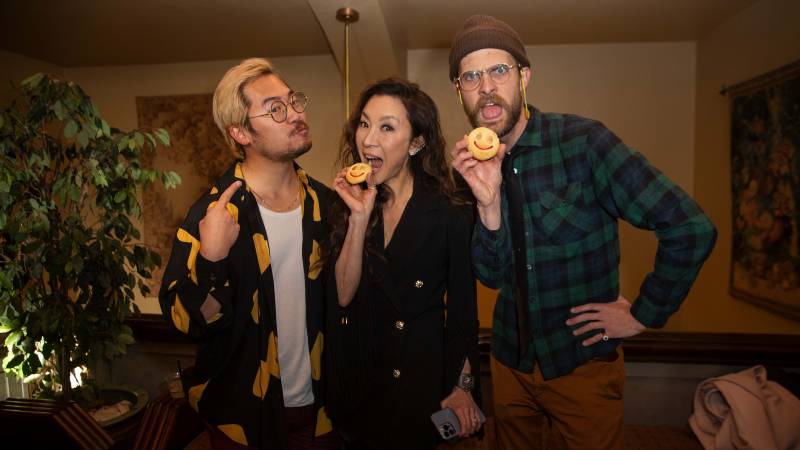 Michelle Yeoh (center) and 'the Daniels' pose with a smiley-faced almond cookie at the Bay Area premiere of their film Everything Everywhere All at Once