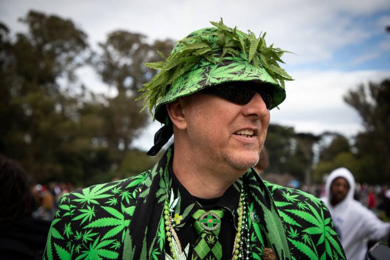 A middle-aged white man wears a suitr and bucket hat adorned with marijuana leaves