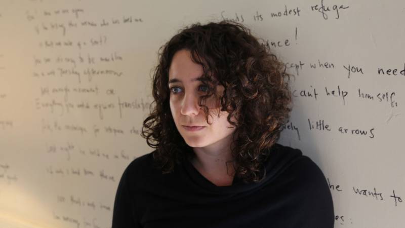 Woman with dark curly hair against white wall covered in writing