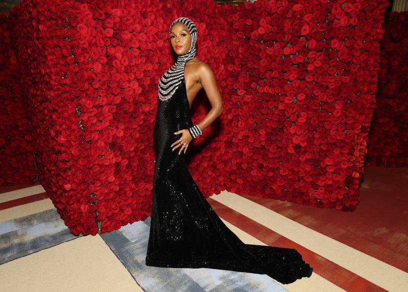 Janeelle Monae in a sleek black gown with short train, low back and a silver hood and chest embellishment.