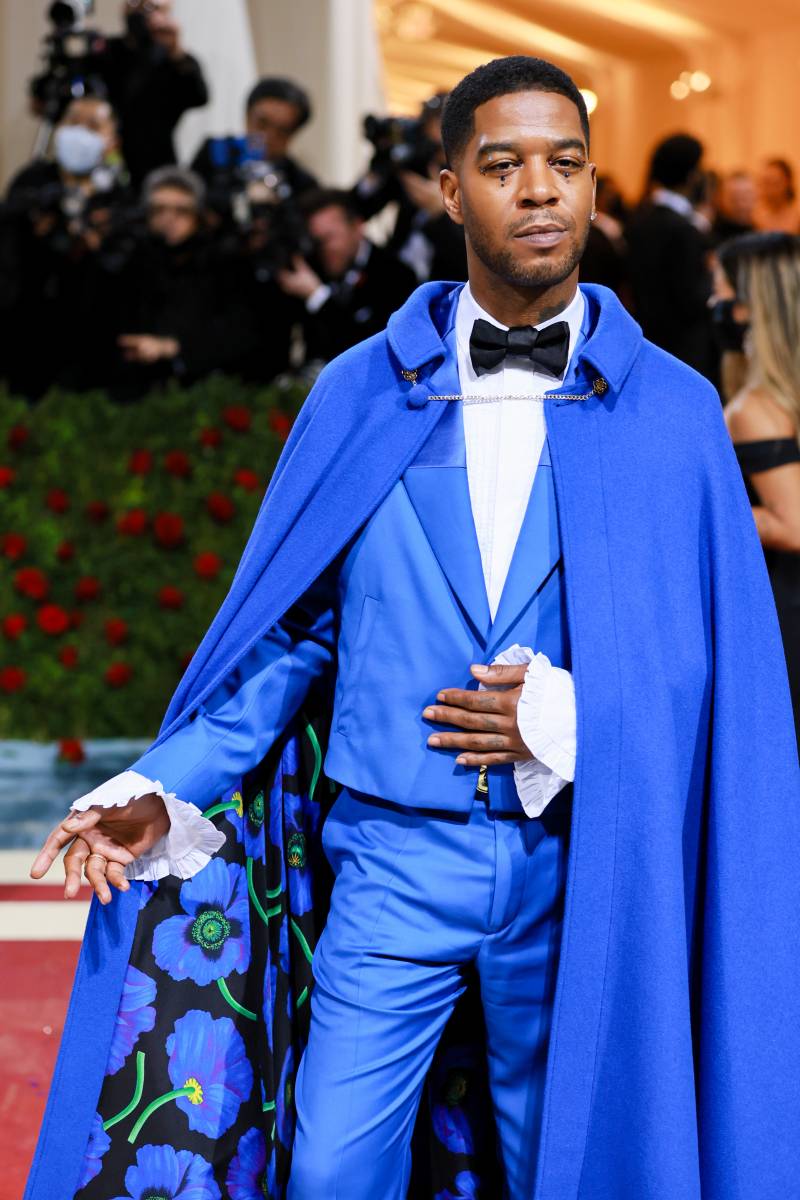 Kid Cudi wearing a white shirt with frilled cuffs, black bow tie, bold blue suit and a matching blue cape.