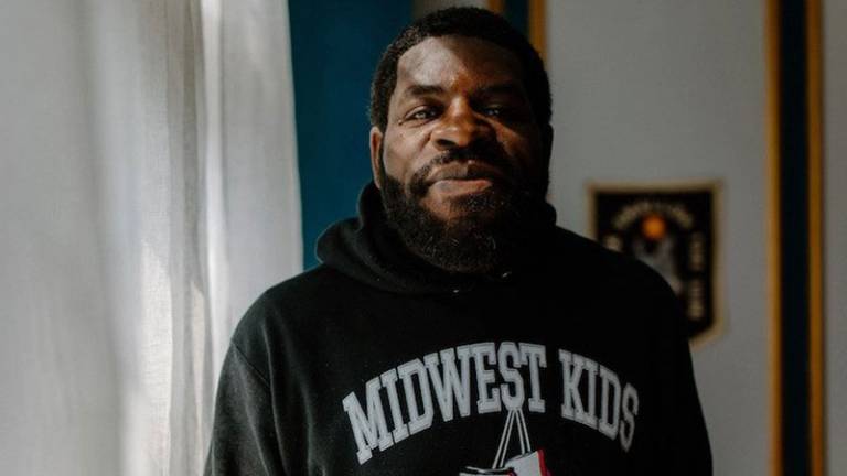 Hanif Abdurraqib in a "midwest kids" sweatshirt, smiling at the camera