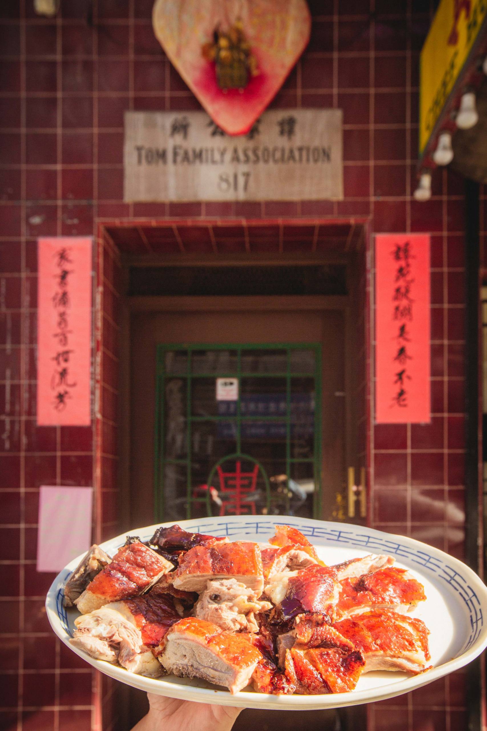 A plate of roast duck held in front of a family association building on Clay Street in San Francisco Chinatown.