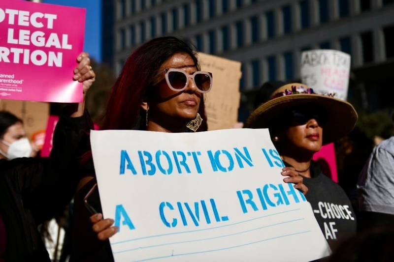 A woman wearing sunglasses stands holding a sign that reads: 'Abortion is a civil right.'