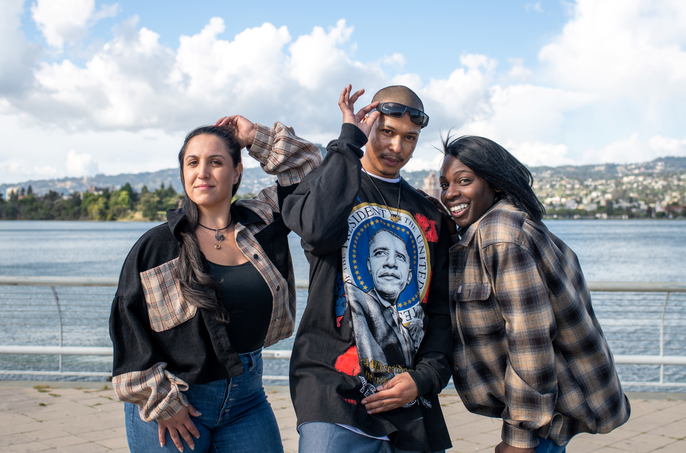 Three people stand in front of Lake Merritt in Oakland and pose while looking at the camera.