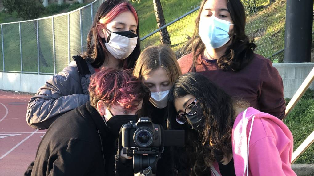 Five young people crowd behind a digital camera