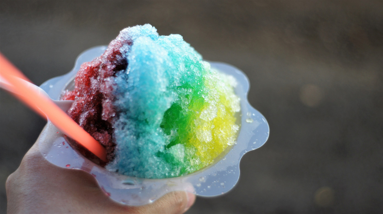 A bowl of Hawaiian shaved ice topped with purple, blue and yellow syrups.