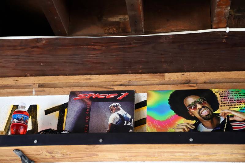 Two music album covers are displayed on a shelf inside the restaurant. One album is of Spice 1, the other is of Mac Dre.