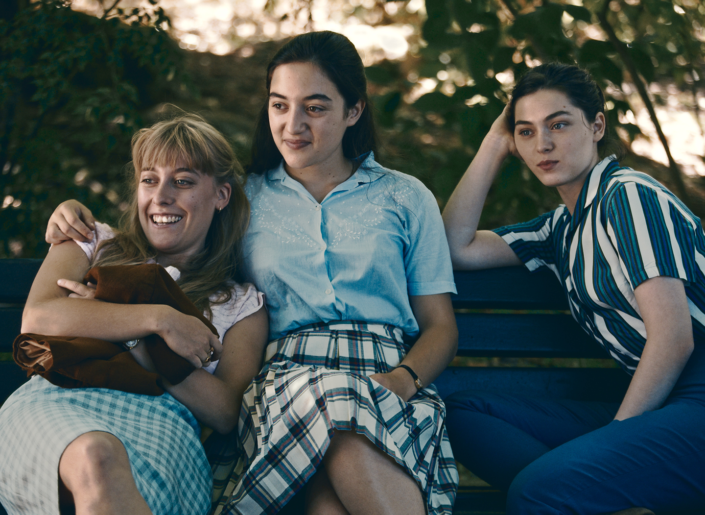 Three young women sit close to each other on a bench