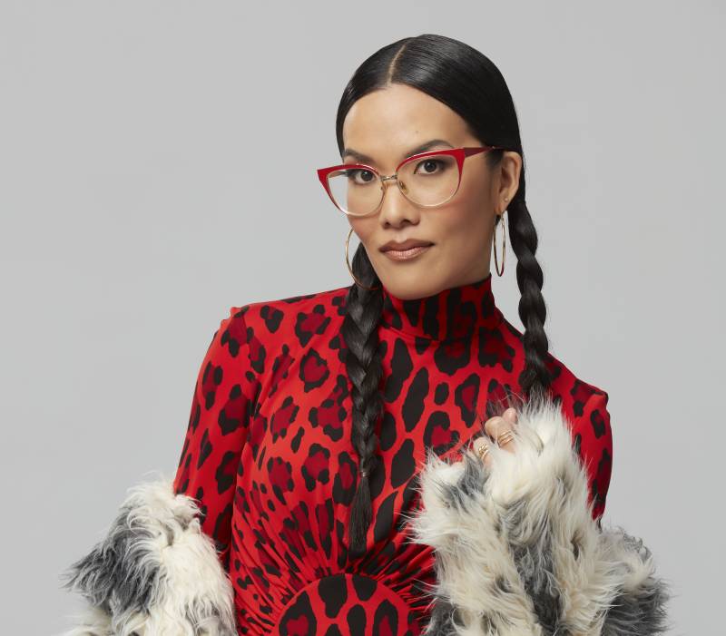 An Asian woman with long hair worn in braids, looks fierce while wearing red eyeglasses and a tight red leopard print top.