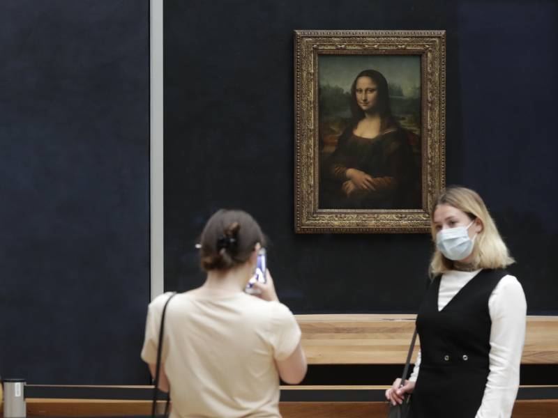 Woman poses next to painting while another woman photographs