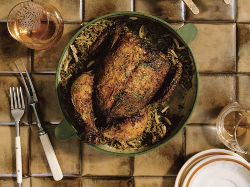 A well seasoned, browned chicken sits in a dish on a tiled surface.