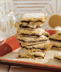 A stack of square cookie bars, drizzled with powered sugar.