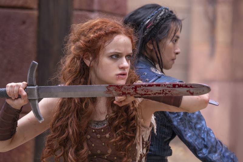 A woman with wild red hair holds a bloody sword aloft as she stands back to back with another woman.