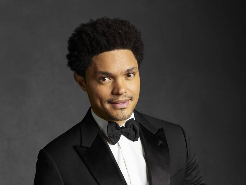 A light-skinned Black man smiles sweetly for the camera, wearing a stylish tuxedo.