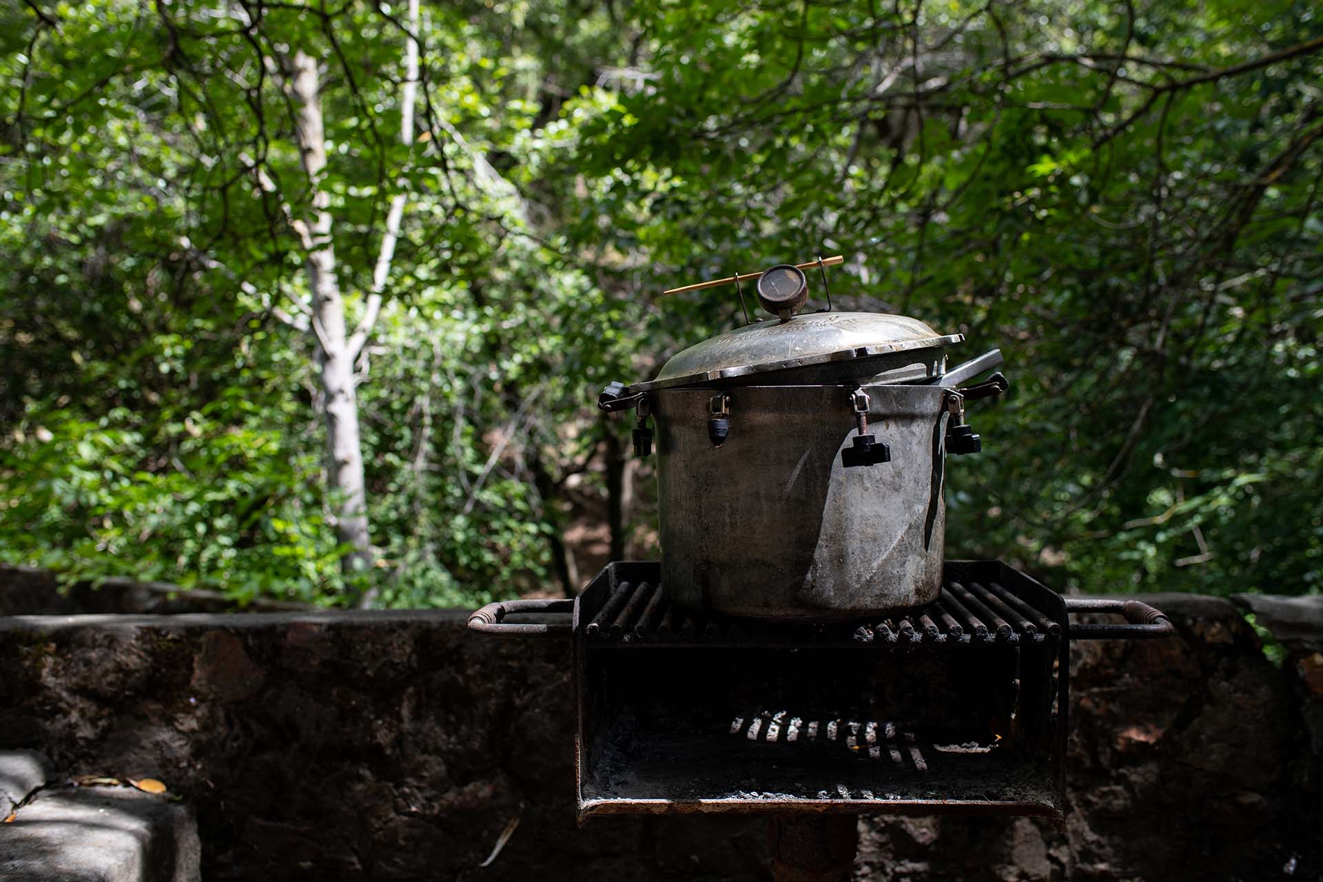 An old pressure cooking sitting on a grill grate, with trees in the background.