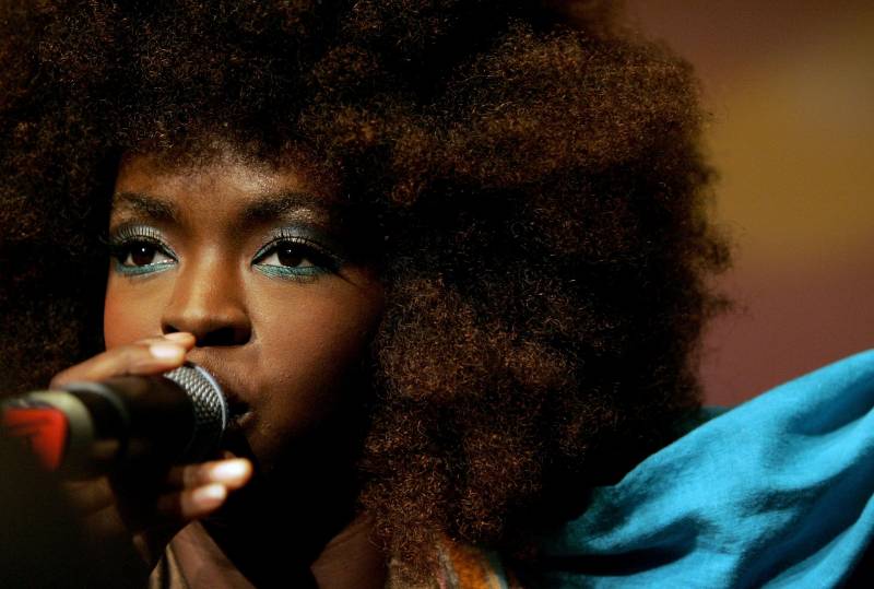 A close-up of a Black woman's face with colorful eyeliner, as she sings into a microphone