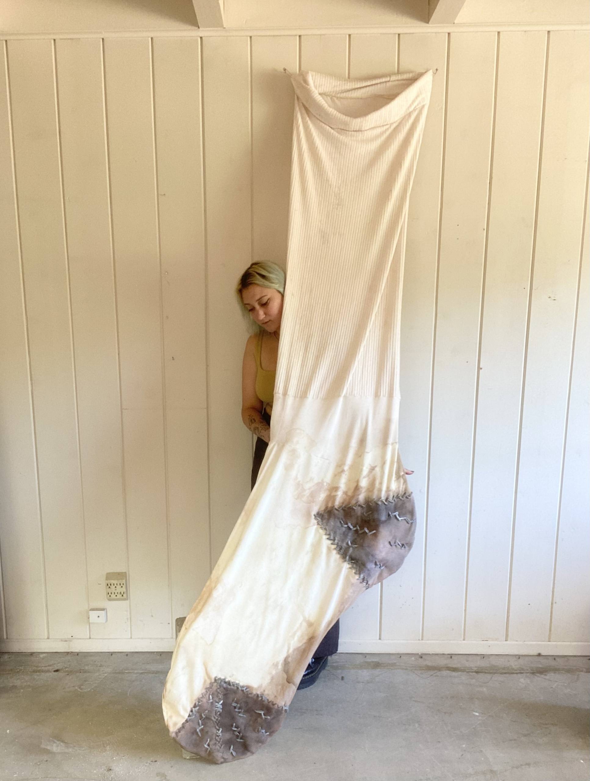 Image of giant white tube sock with shorter artist standing behind it
