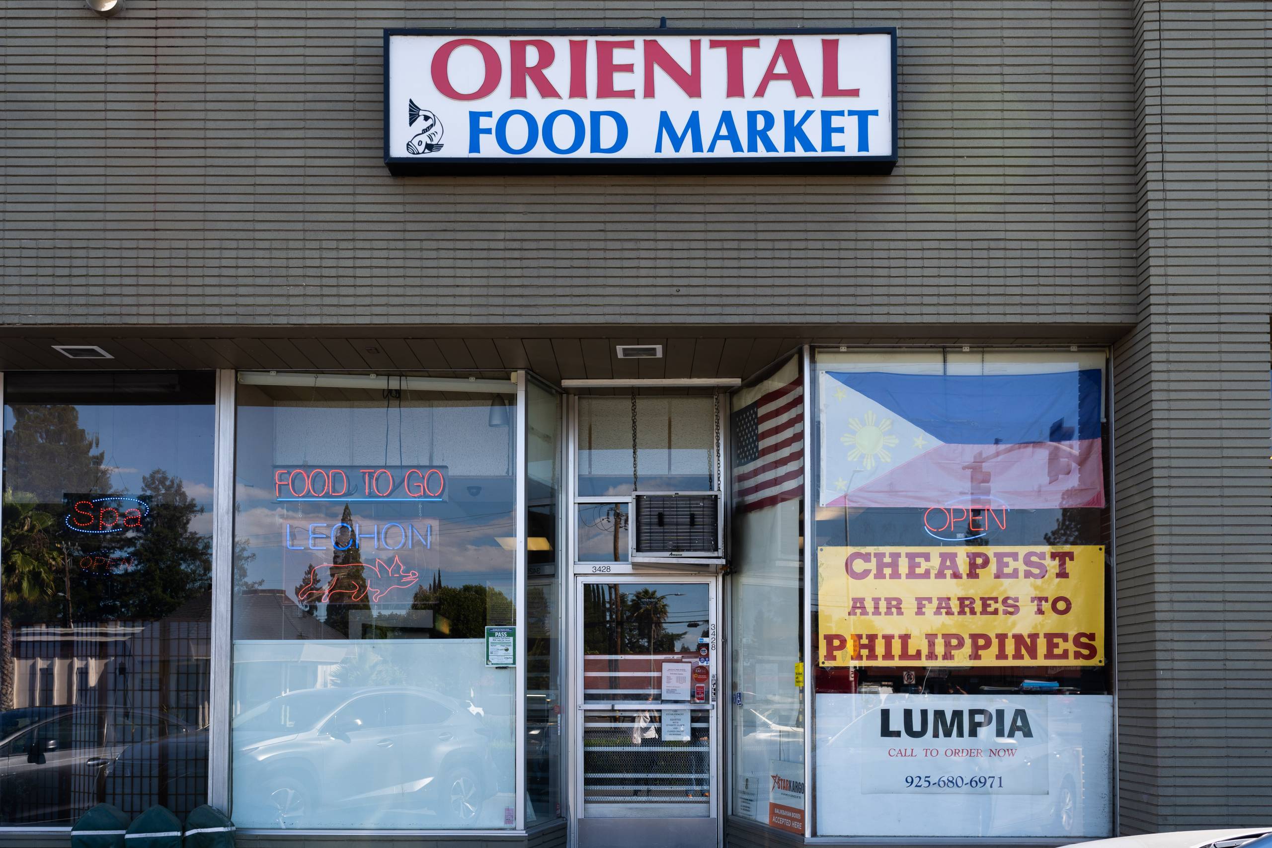 Exterior facade of Oriental Food Market, with signs in the window advertising lumpia and cheap airfare to the Philippines.