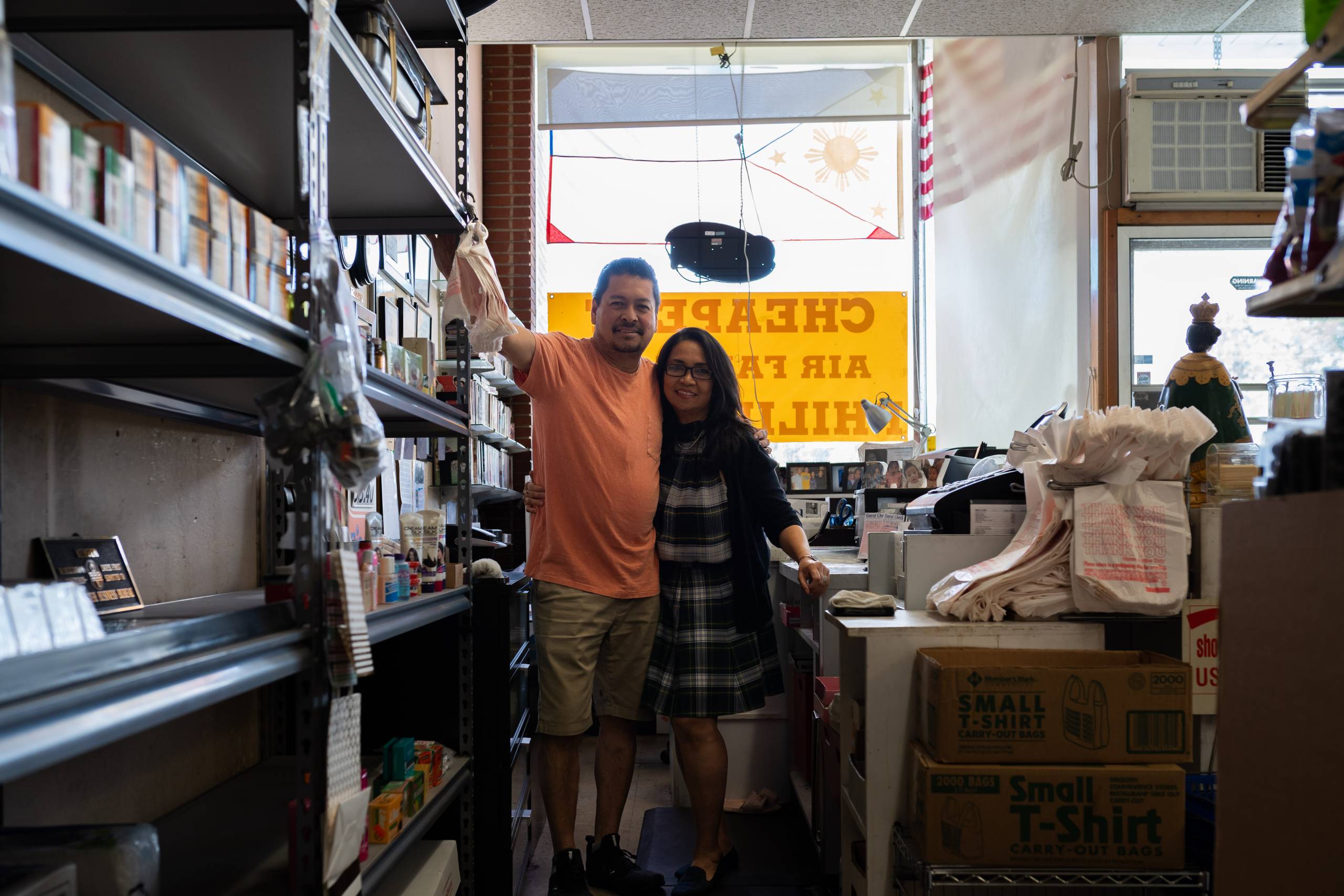 Husband and wife stand behind the front counter of their small Filipino grocer and takeout shop.