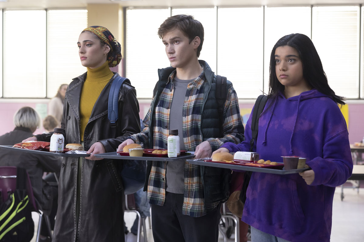 Three teenagers hold cafeteria trays in lunchroom