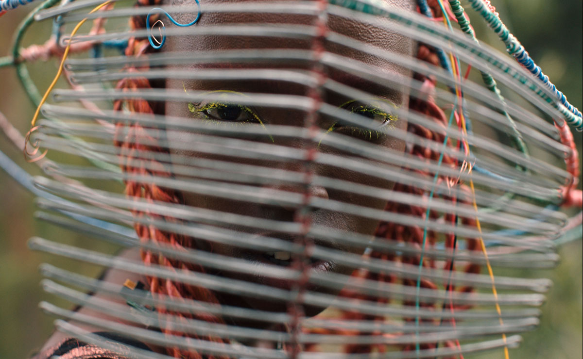 Figure looks at camera through face mask of horizontal wires
