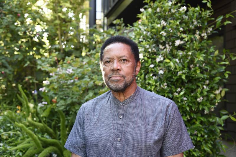 Rodney Barnette stands in front of greenery and flowers in a crisp gray shirt