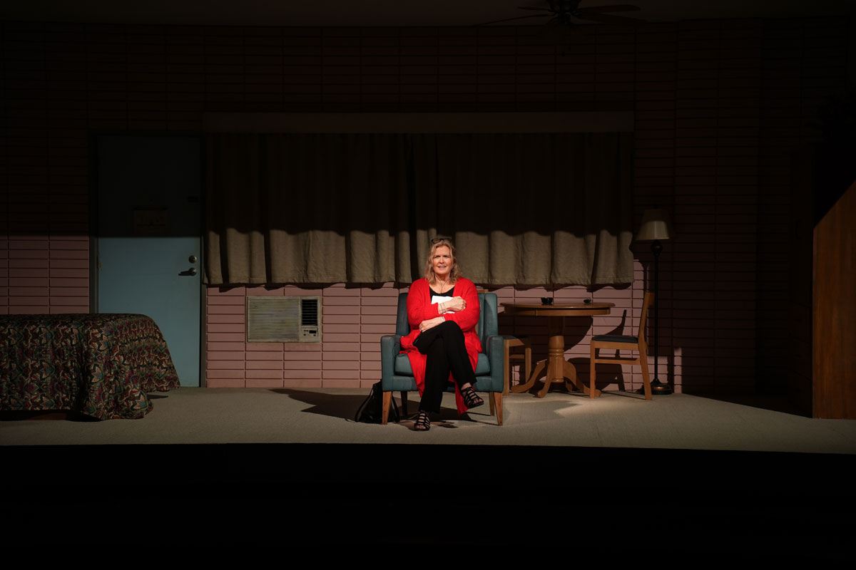 Woman in red sweater sits on a motel-like set