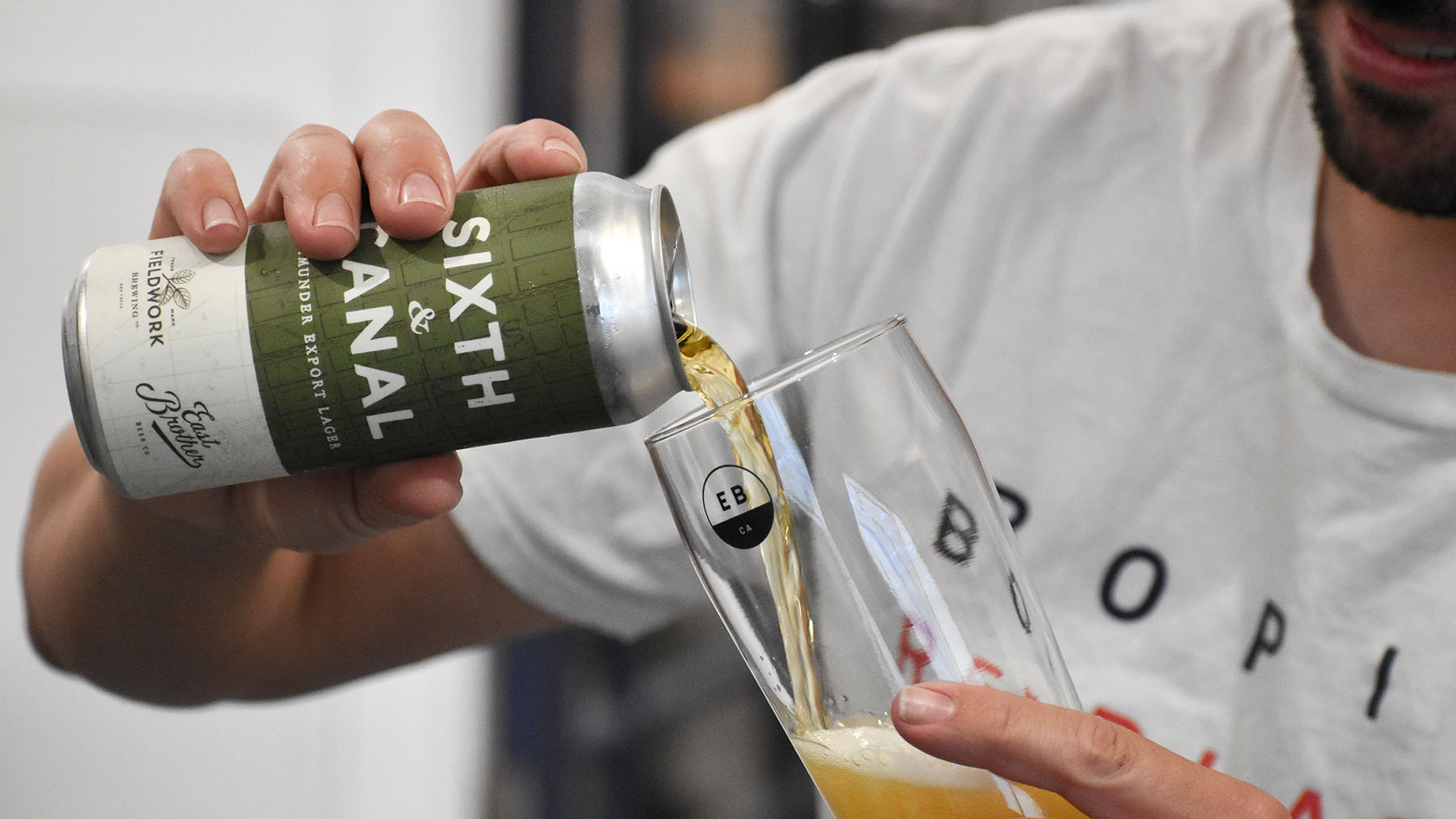 Man pours beer into a glass from a can; the beer label reads "Sixth & Canal."