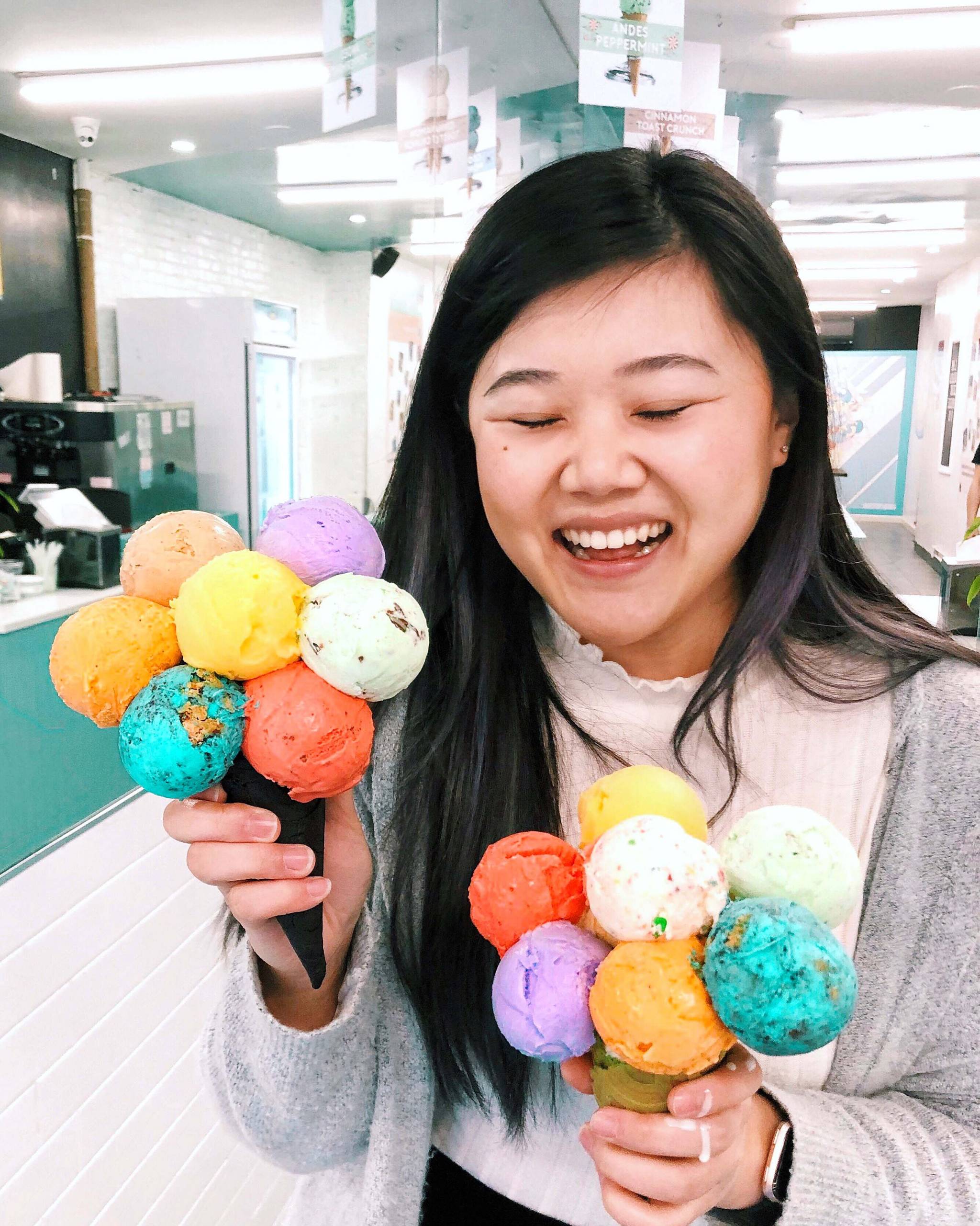 A woman smiles holding a colorful, seven-scoop ice cream cone in each hand.