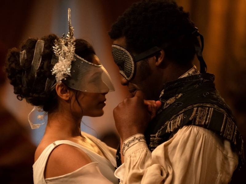 a 19th century couple dances close together at a masquerade ball.