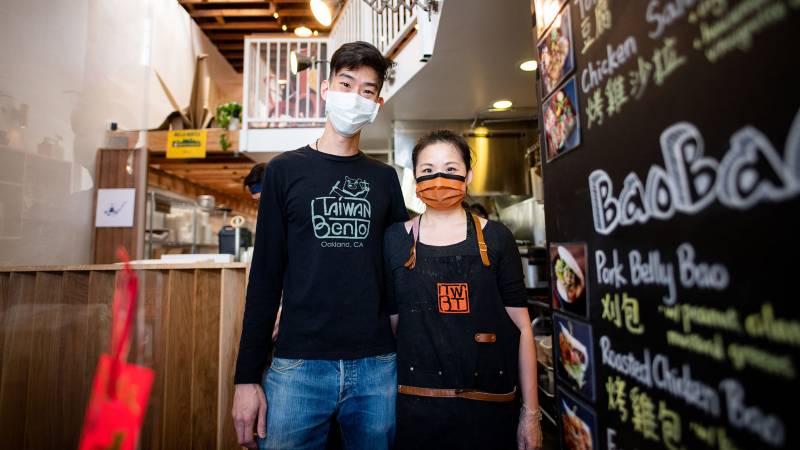 Willy Wang and Stacy Tang, both in face masks, pose inside their Oakland restaurant Taiwan Bento.