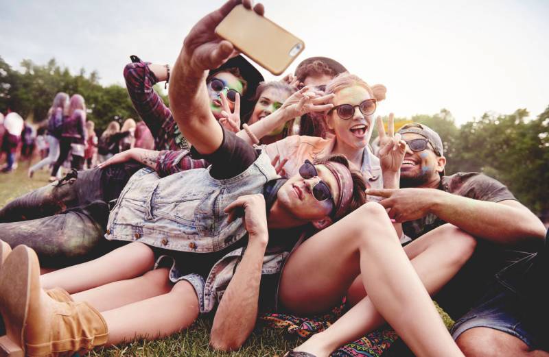 A group of six young friends dogpile for a selfie in a field.